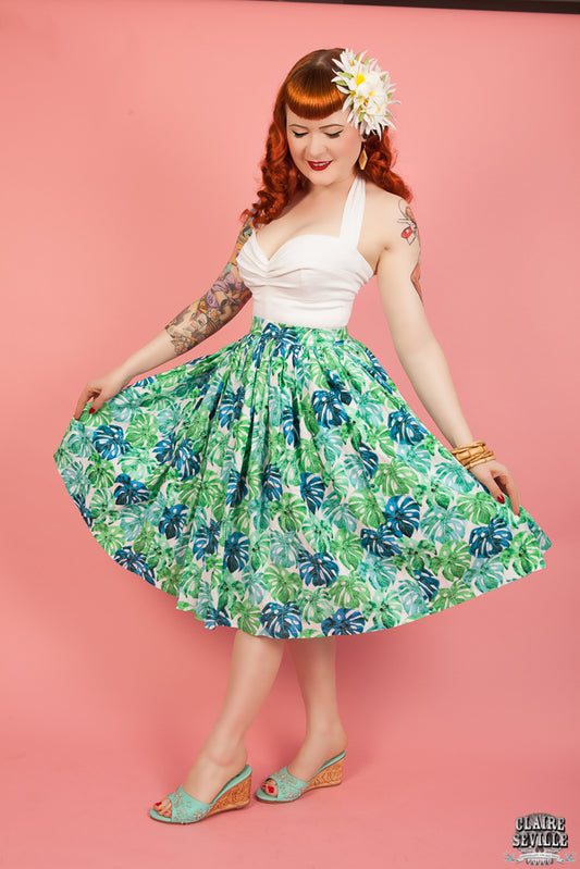 Woman wearing a white top and green floral skirt against a pink background