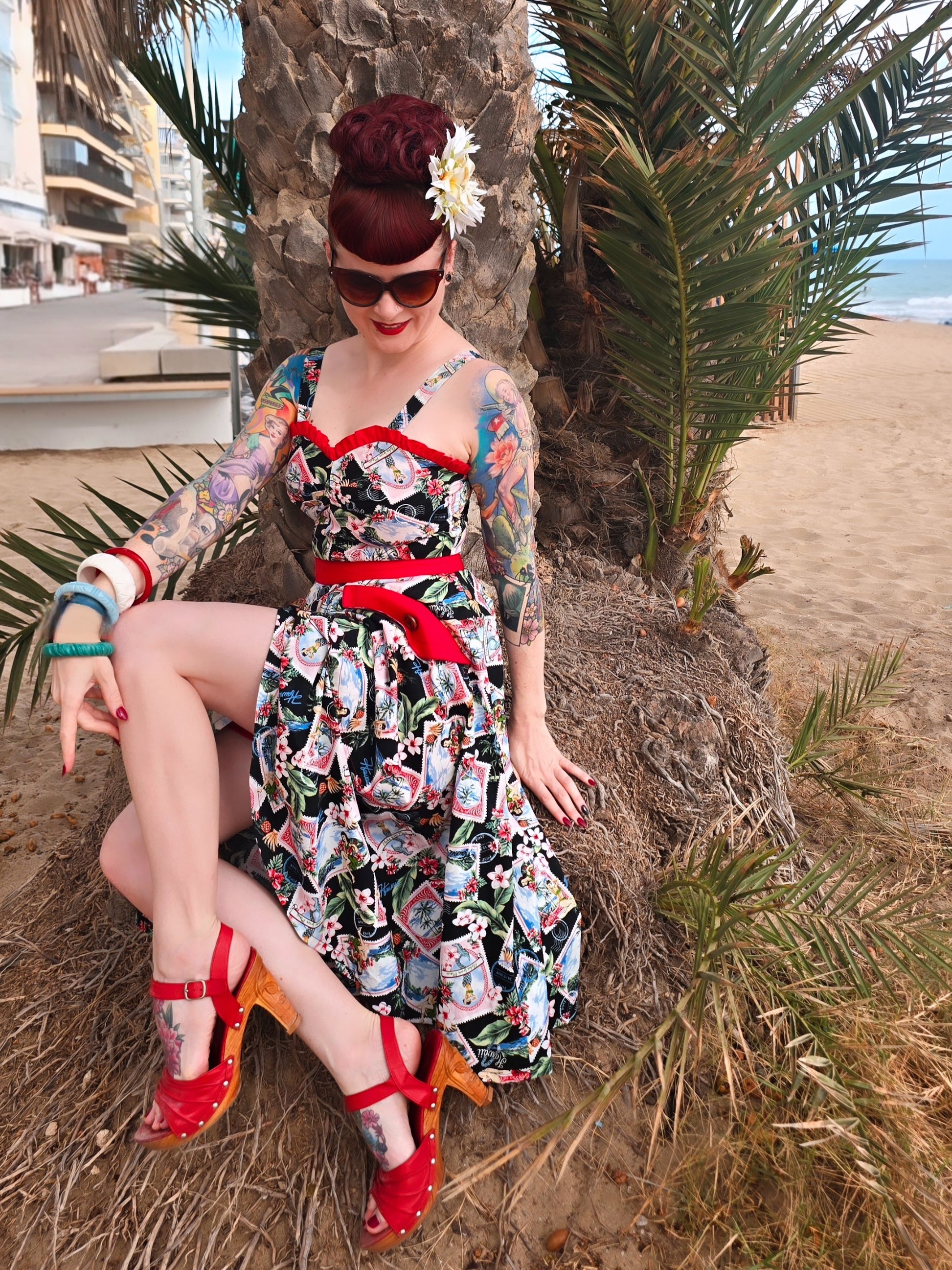 Woman in a colorful dress sitting on a palm tree stump by the beach.