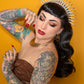 Woman with tattoos and a decorative headpiece against an orange background