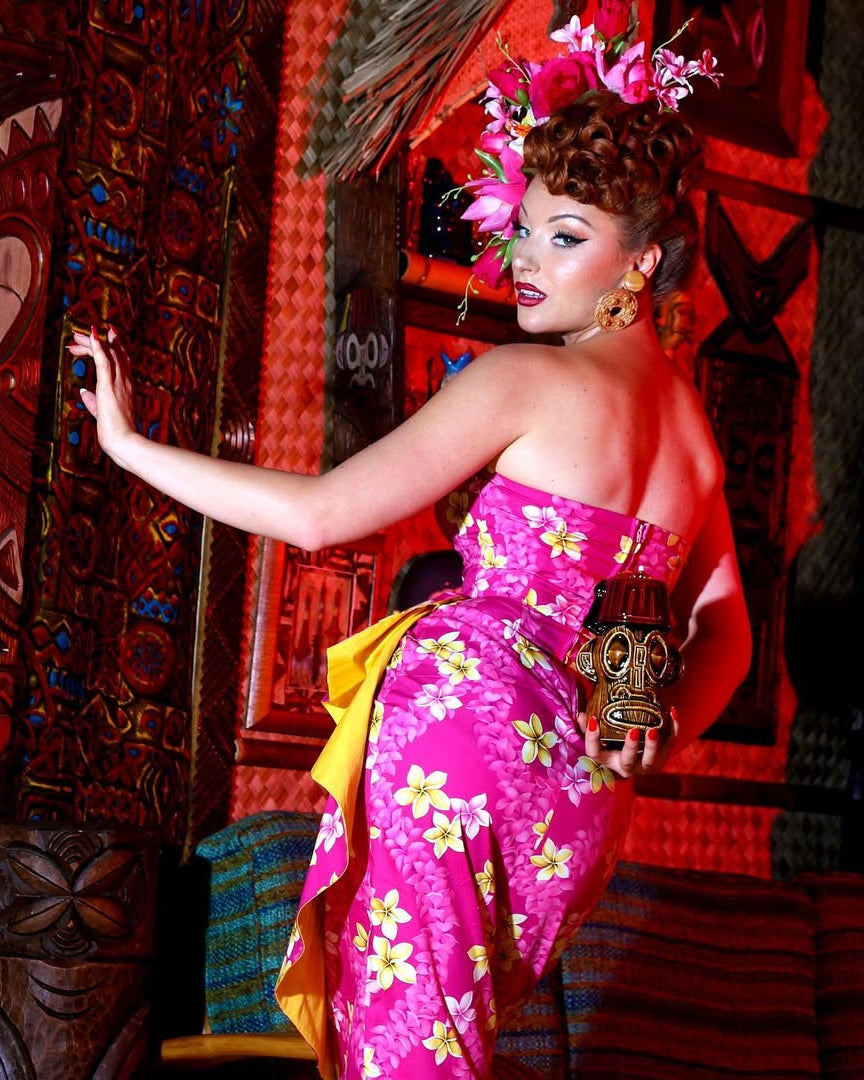 Woman in a vibrant pink floral dress posing in a tropical-themed setting.