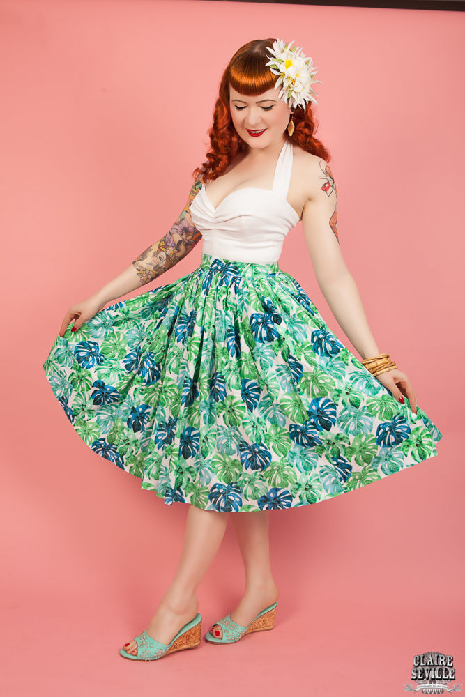 Woman wearing a white top and green floral skirt against a pink background