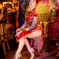 Woman in a red dress with tattoos sitting in a colorful, eclectic room.